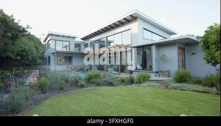 Maison moderne à deux étages située dans un jardin paysagé avec pergola, piscine, pelouse bien entretenue et brume. Contemporain, résidence, verre, patio, feature aquatique Banque D'Images