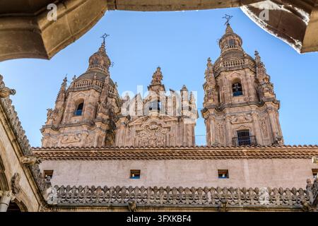 Les deux tours de La Clerecía (église d’un ancien collège jésuite) s’élèvent au-dessus d’un toit de tuiles à Salamanque en Castille-et-León, Espagne. Des arcs de pierre encadrent le ciel en haut, et une bordure ornementale ajourée avec des formes de lys court le long du bas. La vue est prise depuis la cour de la Casa de las Conchas (Maison des Coquilles) en direction de La Clerecía. Le Real Colegio del Espíritu Santo des Jésuites (Collège royal du Saint-Esprit) a été construit entre 1617 et 1754. Aujourd’hui, le bâtiment appartient à l’Université pontificale. Banque D'Images