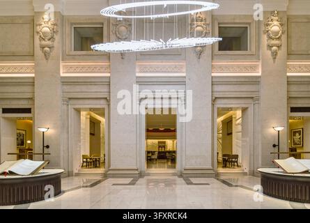 Hall d’accueil au Four Seasons Hotel London à Ten Trinity Square, présentant des ornements en pierre, un sol en marbre et un lustre contemporain frappant. Banque D'Images