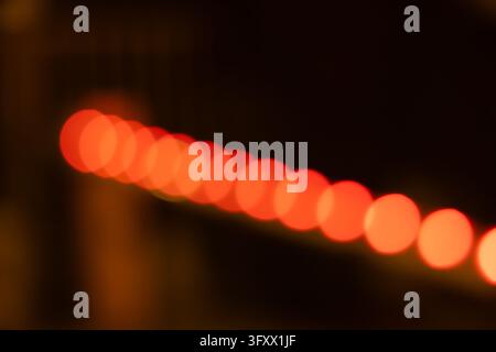 photo abstraite de nuit montrant une séquence diagonale d'orbes de lumière bokeh circulaires, rouges et chauds, flous et doucement lumineux Banque D'Images
