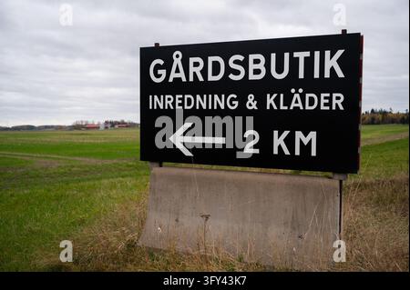 Panneau de signalisation routier faisant la promotion d'une épicerie de ferme suédoise (gårdsbutik) vendant de la décoration intérieure et des vêtements, photographié dans la campagne agricole près de Roa Banque D'Images