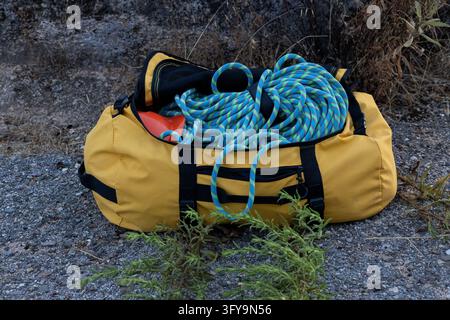 Sac de montagne jaune contenant une corde bleue enroulée et de l'équipement de sécurité sur un terrain rocheux en extérieur Banque D'Images