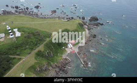 Vue aérienne du phare de Nyudozaki dressé sur une pointe herbeuse avec des falaises rocheuses et une petite jetée s'avançant dans la mer, Oga, Akita, Japon. Banque D'Images