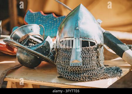 Casque en acier médiéval avec aventail en cotte de mailles reposant à côté d'autres armures sur une table d'exposition en bois, évoquant la guerre historique Banque D'Images