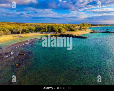 Vue aérienne des eaux turquoise et des sables dorés de Makalawena Beach, encadrés par des roches volcaniques et une végétation côtière luxuriante sous un ciel bleu à Haw Banque D'Images