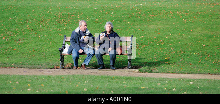 Deux personnes couple assis sur un banc, mangeant à Buxton North England UK UE park Green grass reste de jour d'âge couleur horizontal Banque D'Images
