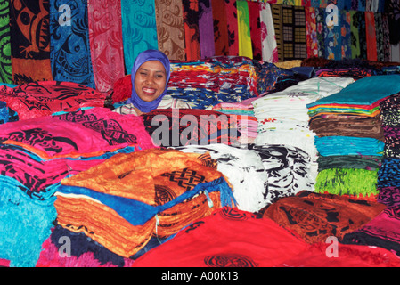 Femme musulmane souriant entouré par une mer de sarongs colorés à la vente à son étal à Seminyak Bali Banque D'Images
