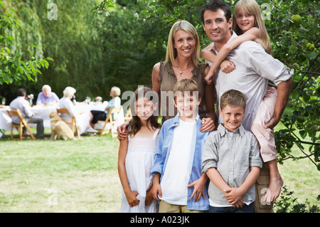 Mid-adult couple et 4 enfants (7-10) en jardin, d'autres membres de la famille en arrière-plan Banque D'Images