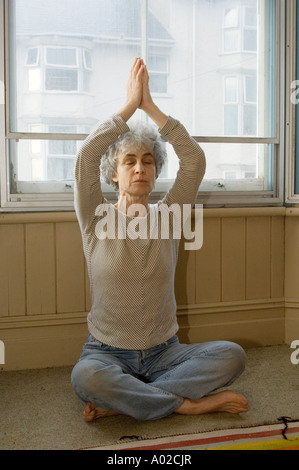 Femme d'âge moyen de pratiquer le yoga à la maison dans la fenêtre de sa maison Banque D'Images