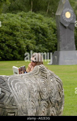 Jeune femme portant des lunettes de lecture livre assis sur un banc en bois sculpté Machynlleth powys Pays de Galles UK central mid Banque D'Images