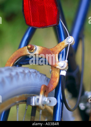 Réflecteur rouge vif et freins rouillé sur un vélo avec des pneus gris bleu. Banque D'Images