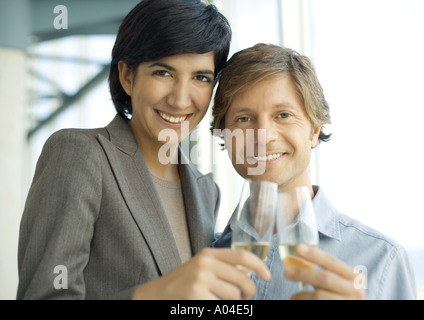 L'homme et de la femme professionnelle tintement des verres de champagne, smiling at camera Banque D'Images