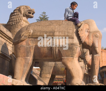 BHAKTAPUR, NÉPAL Népalais Novembre garçon assis sur l'un des éléphants flanquant l'escalier de Nyatapola Mandir Banque D'Images