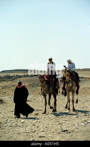 Deux touristes sur camelback et propriétaire d'un chameau dans le désert près des pyramides de Gizeh, Le Caire, Egypte Banque D'Images