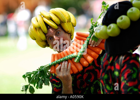 Homme portant des fruits et légumes frais, jouant flûte de pan fait de carottes Banque D'Images