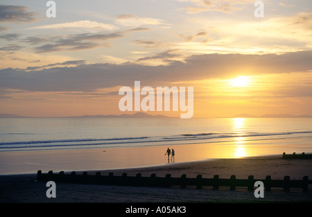 Coucher de soleil sur la plage de la station balnéaire de vacances à Barmouth Gwynedd West Wales, UK. Jeune couple strolling on beach Banque D'Images