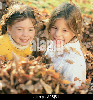 Deux jeunes filles en souriant et jouant dans un tas de feuilles avec les feuilles sur leurs chandails et dans leurs cheveux Banque D'Images