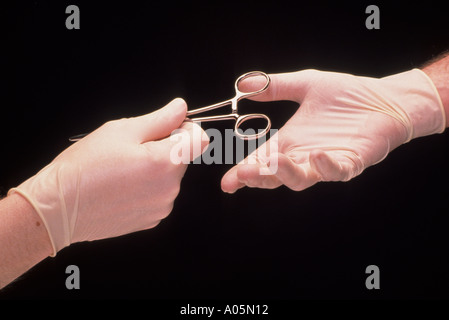 Gros plan d'une paire de mains passant un hemostat chirurgien pendant l'intervention Banque D'Images