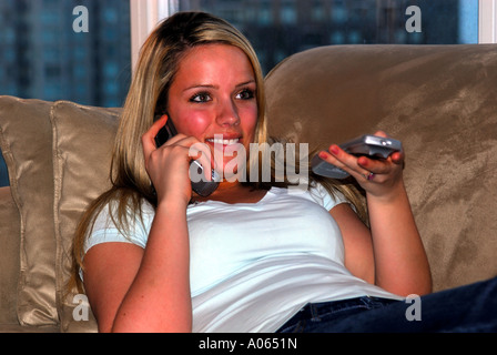 20 ans vieille femme à la maison à regarder la télévision tout en prenant le téléphone Banque D'Images