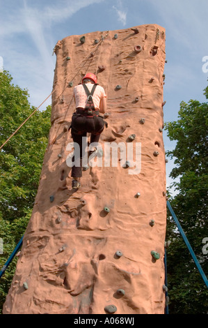 Un homme grimpant un mur de roche monolithique portant un casque de sécurité et un harnais sur un fond de ciel bleu clair. Banque D'Images