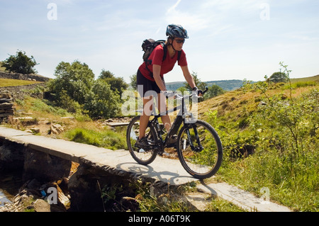 Vélo de montagne femelle sur l'ancien pont de pierre entre Clapham et dans le Yorkshire Dales Austwick Banque D'Images