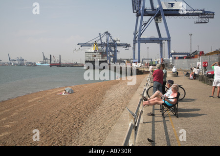 Porte-conteneurs et de grues Felixstowe docks avec les gens sur la plage et profiter du soleil assis sur des bancs, Suffolk, Angleterre Banque D'Images