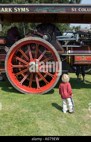 Un petit enfant « moderne » se tient devant une grande roue sur un moteur de traction à vapeur « ancien » au Royal Cornwall Agricultural Show Wadebridge Angleterre Royaume-Uni Banque D'Images