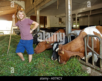 Jeune agriculteur dans l'alimentation des vaches avec étable foin frais Banque D'Images