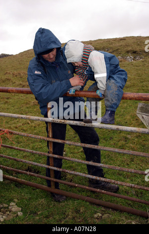 Père Fils aidant à franchir la porte d'un agriculteur en marchant dans le Yorkshire Dales Banque D'Images