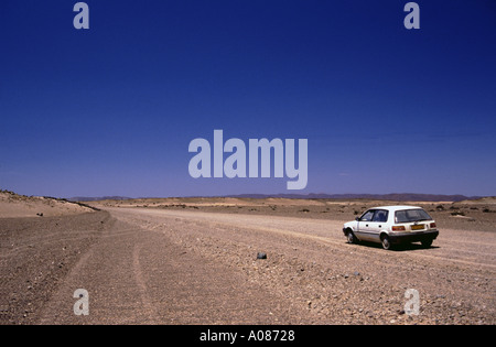 Voiture blanche sur une route du désert solitaire de gravier dans la rue sans fin du désert de Namibie seul sec Banque D'Images