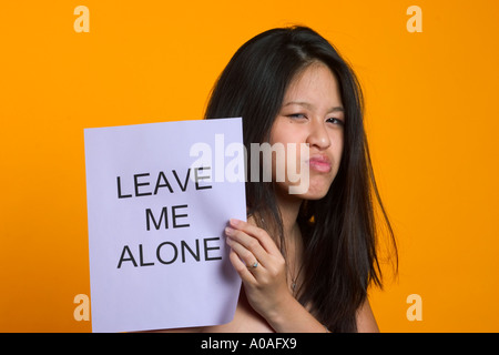 Young Asian woman holding a sign reading, 'laisse-moi tranquille". Banque D'Images