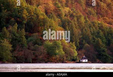 Rivage de Loch Cluanie Highlands écossais pentes boisées banque en lumière du soir avec petite propriété sur l'eau Banque D'Images