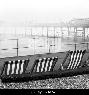 Trois transats rayé Mono sur promenade jour brumeux avec pier disparaissant dans la brume Teignmouth Devon du sud Banque D'Images