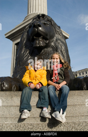 Des enfants assis à l'une des sculptures de lion par Sir Edwin Landseer à Trafalgar Square London England UK Banque D'Images