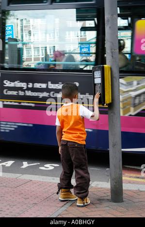 En appuyant sur le bouton de l'enfant sur un panneau de contrôle à un pélican crossing, attendant de traverser une route dans une ville anglaise. Banque D'Images