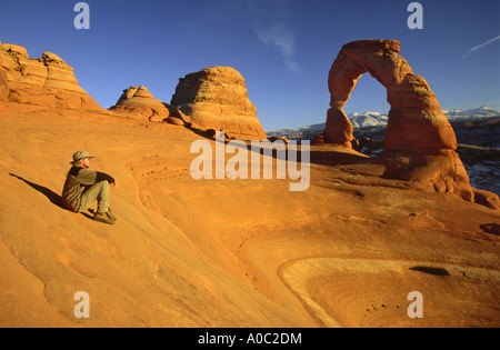 Randonneur près de Delicate Arch en hiver, La Sal Mts en dist, Arches nat Park, Utah, USA Banque D'Images