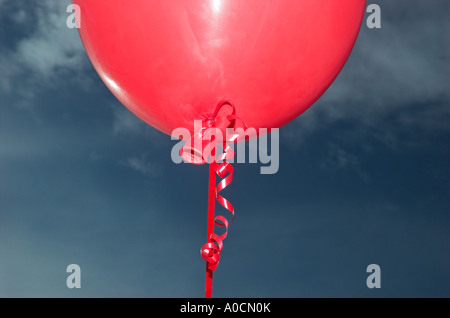 Fermer la vue d'un ballon rouge attaché avec un ruban frisé against sky Banque D'Images