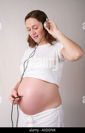 Très jeune femme enceinte au troisième trimestre utilise un casque branché à ses forces navales d'écouter son bébé enfant drôle Banque D'Images