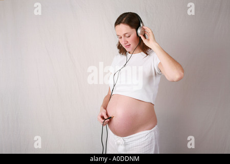 Très jeune femme enceinte au troisième trimestre utilise un casque branché à ses forces navales d'écouter son bébé enfant drôle Banque D'Images