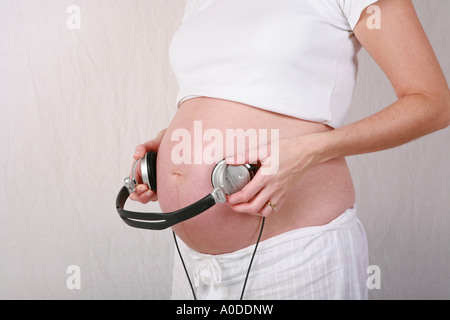 De gros plan femme enceinte lourdement dans l'estomac le troisième trimestre avec des écouteurs à jouer de la musique à bébé foetus in utero de l'enfant Banque D'Images