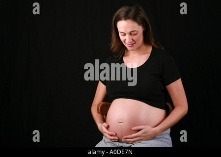 Femme enceinte 34 semaines assise sur un tabouret la réconforte bébé enfant fœtus avec les mains sur l'estomac par tapotement Banque D'Images