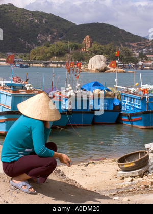 Vietnam Nha Trang city port de pêche de la rivière Cai femme portant Chapeau conique traditionnel squatting on riverbank Banque D'Images