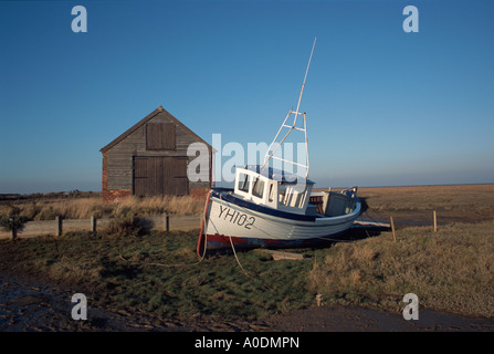 Un bateau de pêche côtière hors de l'eau et l'ancienne grange du charbon par le port de Thornham, Norfolk, Angleterre, Royaume-Uni, Europe. Banque D'Images