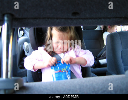 Jeune fille enfant en ayant accès de colère dans la tentative d'ouverture du siège d'auto sachet de bonbons Banque D'Images