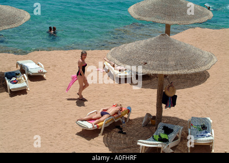 Une femme d'âge moyen les promenades le long de la plage à Sharm el Sheikh, Naama bay, avec le soleil et les nageurs autour d'elle. Banque D'Images