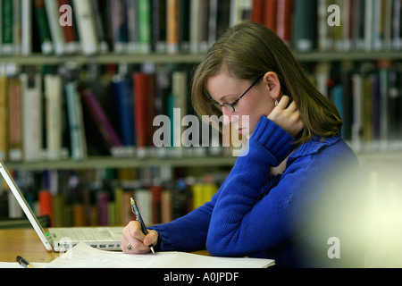 Jeune femme étudiante travaillant dans une bibliothèque séjour jeune femme travaillant dans une bibliothèque à une affectation sur un sujet donné Banque D'Images