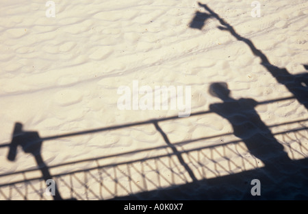 Ombres projetées sur sable blanc et doux de l'homme en été hat s'appuyant sur les garde-corps et de station télescope et pôle d'éclairage Banque D'Images