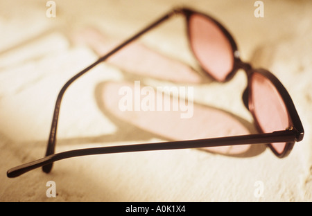 Une paire de lunettes teintées de rose jette une ombre sur une surface blanche texturée Banque D'Images