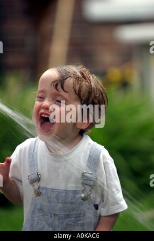Lewis âgés de deux à jouer avec l'arrosage dans le jardin Banque D'Images