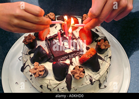 Éclairage mains des bougies sur un gâteau au chocolat avec des fraises Banque D'Images